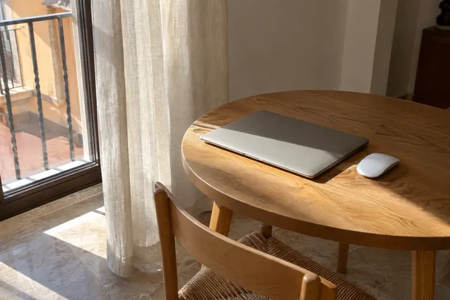 Ordenador portátil cerrado y ratón en una mesa junto a una ventana